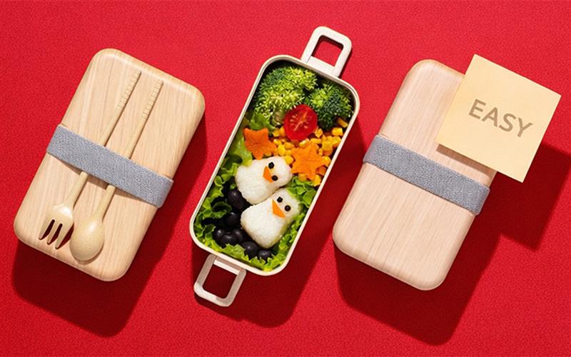 An image showing an easy bento box meal with penguin-shaped rice balls and colorful vegetables on a red background, illustrating a simple meal-prep concept.