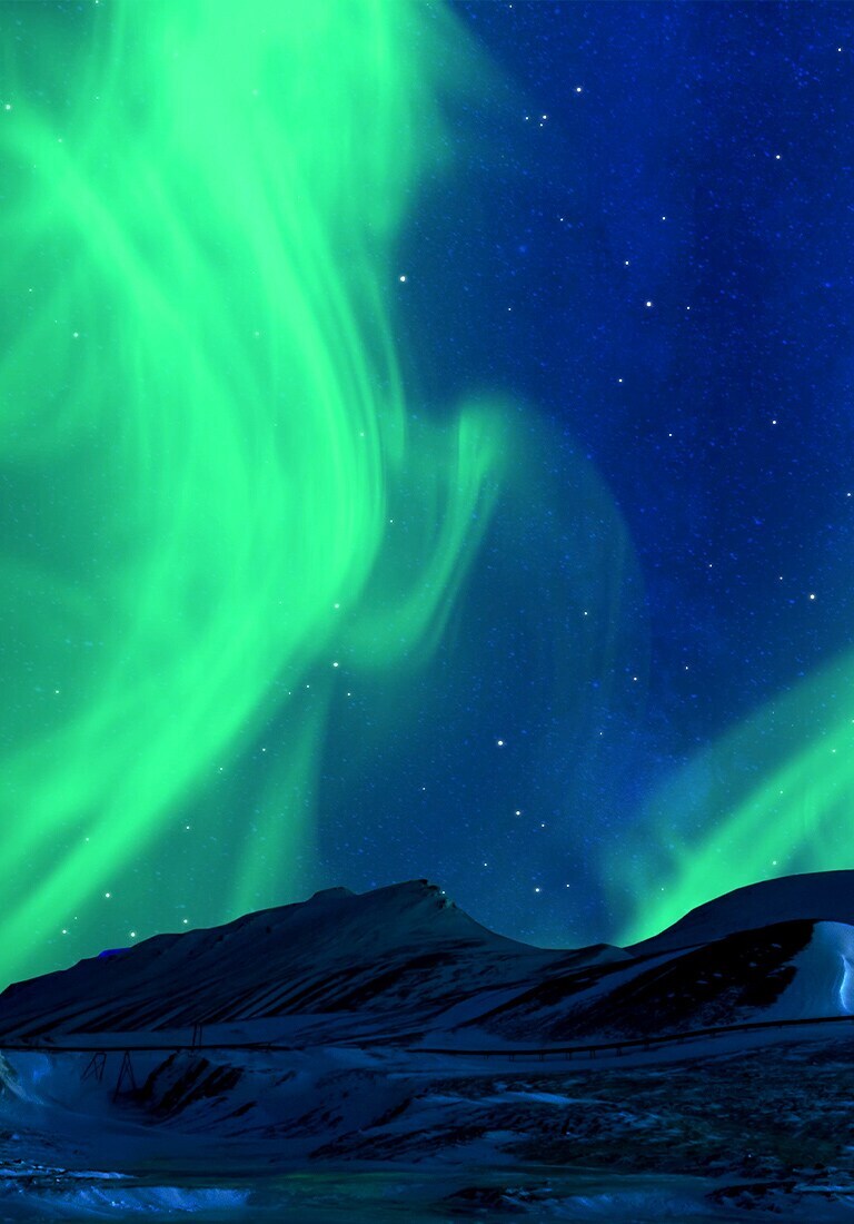 Winter landscape of snowy mountains with starry night sky and green polar lights in the background.