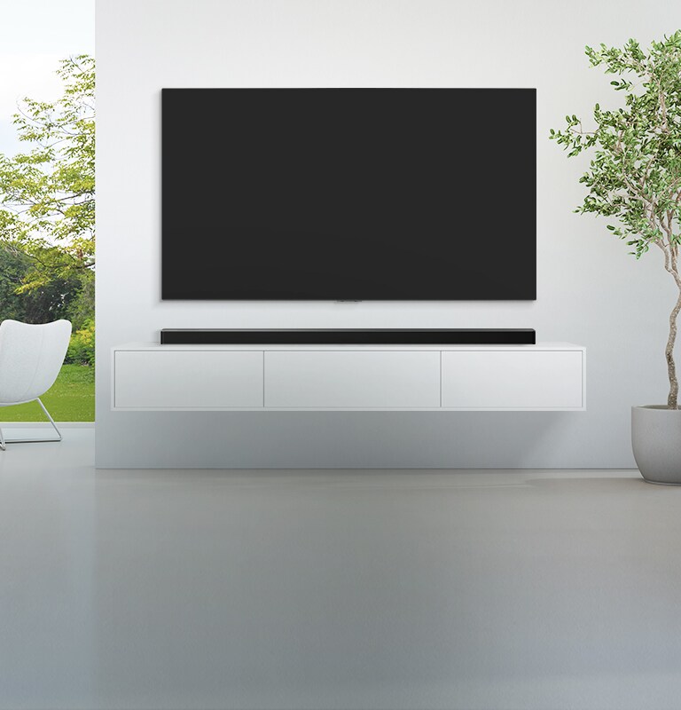A TV and a soundbar are placed in a wide, white living room, and there is a green forest view outside seen from the wide window. 