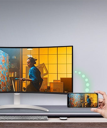 A monitor is placed on the table, and to the right, a phone displaying the same screen as the monitor is visible.	