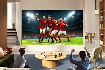 La télévision LG pour les amateurs de sport est montée au mur dans un salon lumineux, montrant une célébration de soccer aux couleurs vives et à une qualité d’image raffinée sur un grand écran, tandis qu’une famille assise sur des sofas acclame ensemble.