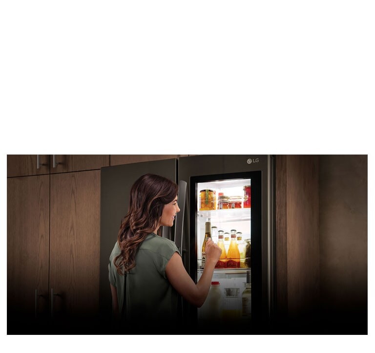 Une femme se tient devant un réfrigérateur avec un verre de jus à la main. Elle sourit en fermant la porte.