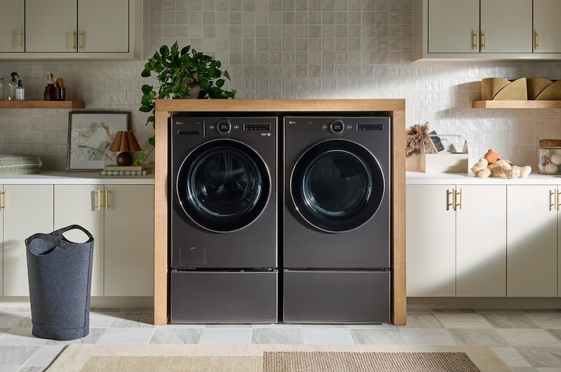 L'ensemble lave-linge et sèche-linge frontal LG (WM6700HBA) en Noir Acier, présentant une installation côte à côte élégante sur des socles, intégrée dans un mobilier moderne.