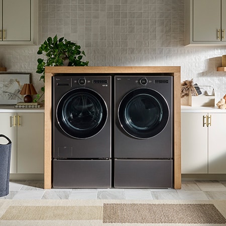 La sécheuse LG DLEX6700B de 7,4 pi³ en acier noir, installée côte à côte avec une laveuse assortie sur des socles dans une buanderie moderne.