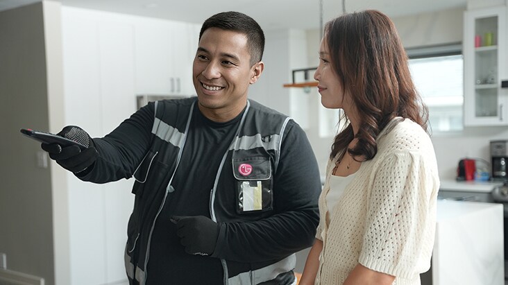 Technicien de LG souriant, expliquant quelque chose à un client dans une cuisine moderne et lumineuse, représentant le service à domicile de LG et les réparations à prix forfaitaire.