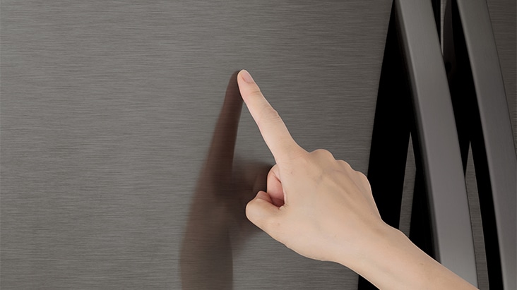Un doigt touchant la surface en acier inoxydable brossé gris foncé d'un réfrigérateur sans laisser de traces.