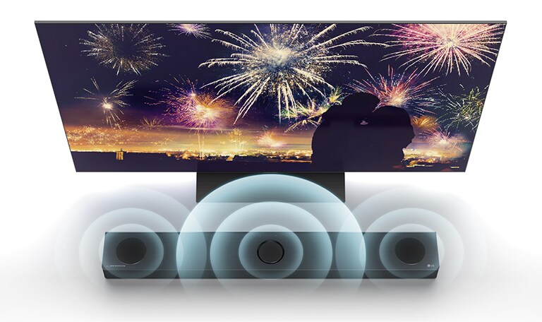 En vue d’ensemble, un téléviseur de LG est posé au sol et une barre de son de LG se trouve juste en dessous, dans l’espace infini. À l’écran du téléviseur, la silhouette d’un couple se dessine sur un fond de feux d’artifice. Les graphiques de l’onde sonore proviennent des haut-parleurs central, gauche et droit de la barre de son supérieure.