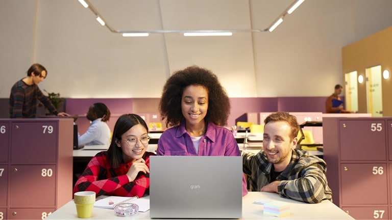 Trois personnes dans le bureau regardent un gramme en souriant.