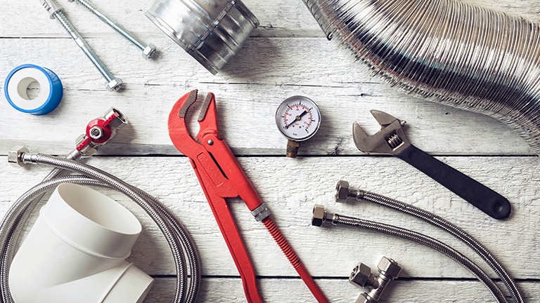 Sur un plancher en bois blanc, une variété d’outils et de fournitures sont disposés, avec une clé à molette rouge au centre de l’attention.