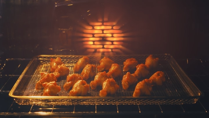Ailes de poulet dorées cuisant sur une grille métallique à l'intérieur d'un four chaud et éclairé.