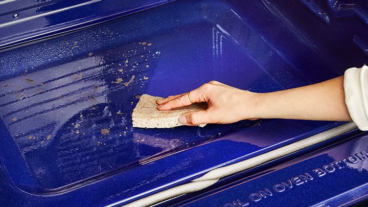 Une main utilisant une éponge pour nettoyer l'intérieur bleu d'un four.