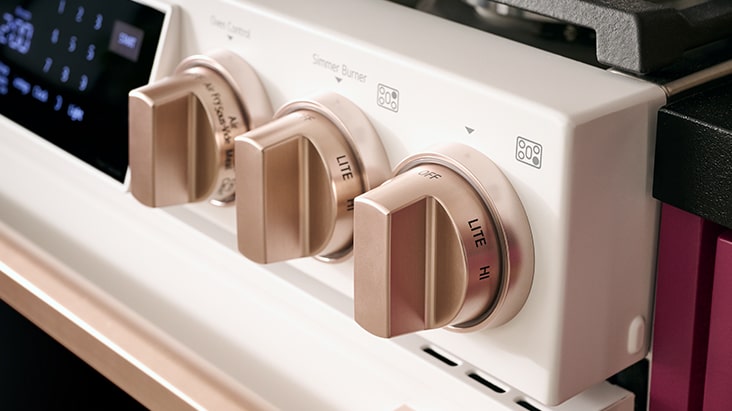Gros plan sur les boutons de commande rotatifs en métal doré d'une cuisinière blanche moderne.