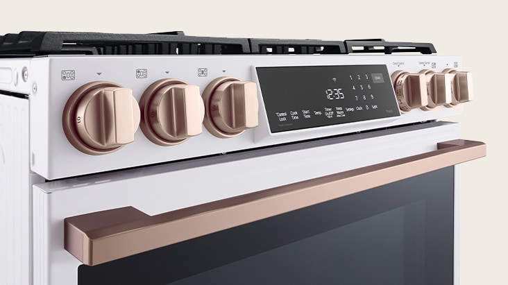 Cuisinière blanche moderne avec boutons et poignée en cuivre, dotée d'un panneau de commande numérique tactile.
