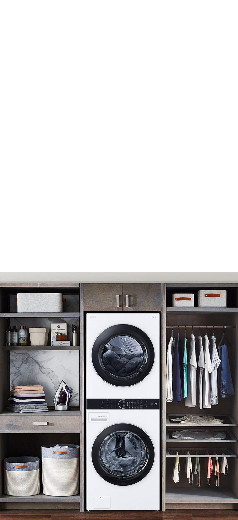 Machine à laver LG blanche encastrée au centre, entre placards, vêtements suspendus à droite, paniers en bas.