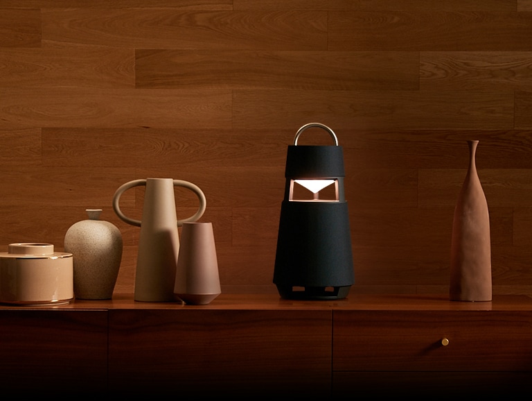 Image du haut-parleur XBOOM 360 avec des sculptures sur une meuble dans un intérieur aux tons boisés.