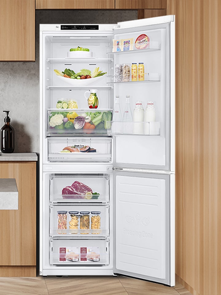 Réfrigérateur combiné blanc ouvert rempli d'aliments frais, intégré dans une cuisine moderne en bois.