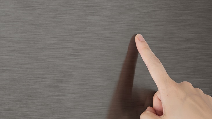 Un doigt touchant une surface lisse en acier inoxydable brossé gris foncé sans laisser de traces.