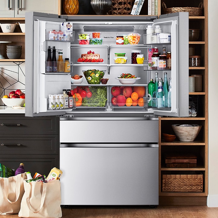 Réfrigérateur en acier inoxydable à portes françaises ouvert, rempli d'aliments frais dans une cuisine moderne.