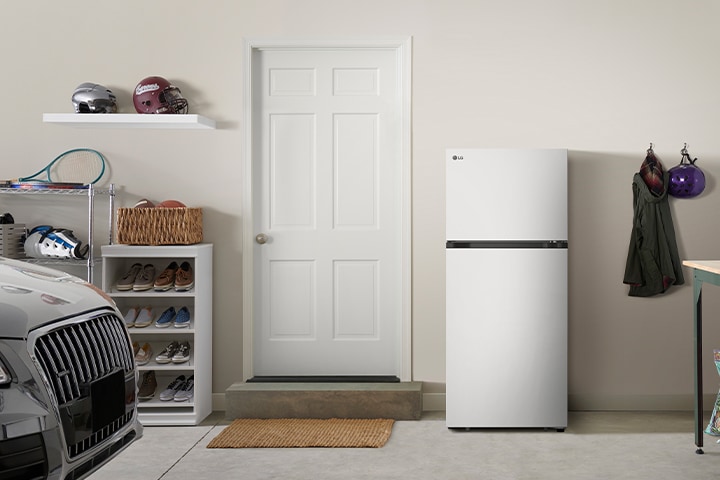 Réfrigérateur LG blanc à deux portes installé dans un garage à côté d'une porte d'entrée blanche.