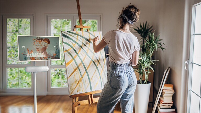 Le StanbyME de LG est placé dans un salon et le haut-parleur XT7S y est fixé. Une femme dessine tout en écoutant de la musique grâce à l’écran et au haut-parleur combinés.