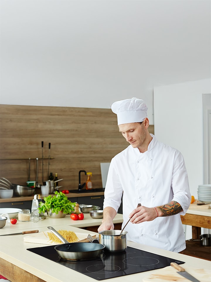 Un chef professionnel utilise une casserole sur une surface de cuisson à induction noire et élégante dans une cuisine moderne, mettant en évidence la précision et l’efficacité de la technologie à induction.