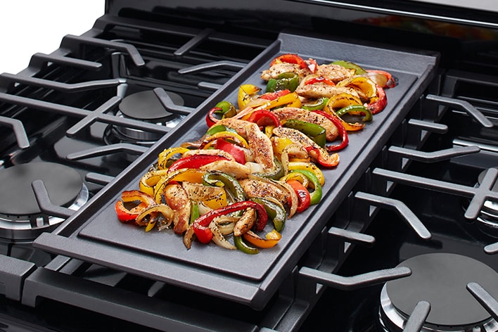 Tranches de bacon cuisant sur une plaque chauffante intégrée d'une cuisinière à gaz en acier inoxydable.
