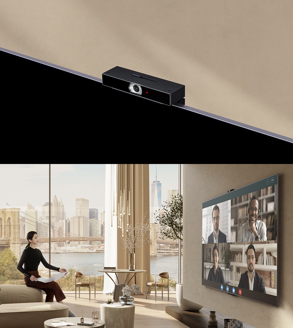 Une femme est assise sur l’accoudoir d’un canapé, tenant un ordinateur portable et regardant un téléviseur. À l’écran du téléviseur, on peut voir quatre personnes et une vidéoconférence.