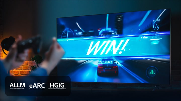 Dans un jeu de course automobile, la voiture du joueur passe la ligne d’arrivée et gagne la course. En avant-plan, le joueur tient dans les mains la manette. Les logos MAFL, eARC et HGiG sont affichés dans le coin inférieur gauche.