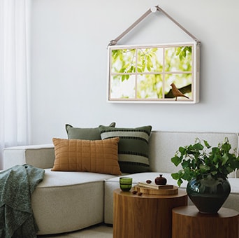 L’écran mobile StanbyME 2 Max LX6 de LG est présenté comme un écran installé au mur dans un salon moderne, montrant un paysage au-dessus d’un canapé et d’une table en bois, mettant en valeur un écran détachable et portatif.