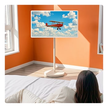 LG StanbyME 2 Max LX6 Movable Screen is placed in a bright room with orange walls beside a window, displaying a red airplane flying across a blue sky, highlighting vivid screen content and flexible placement for relaxed viewing.