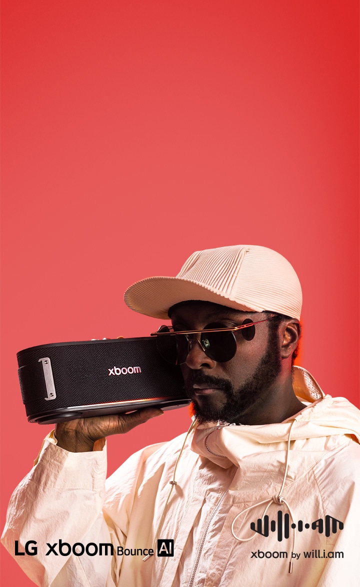 will.i.am, vêtu de blanc et portant des lunettes de soleil, tient la XBOOM Bounce près de son visage.