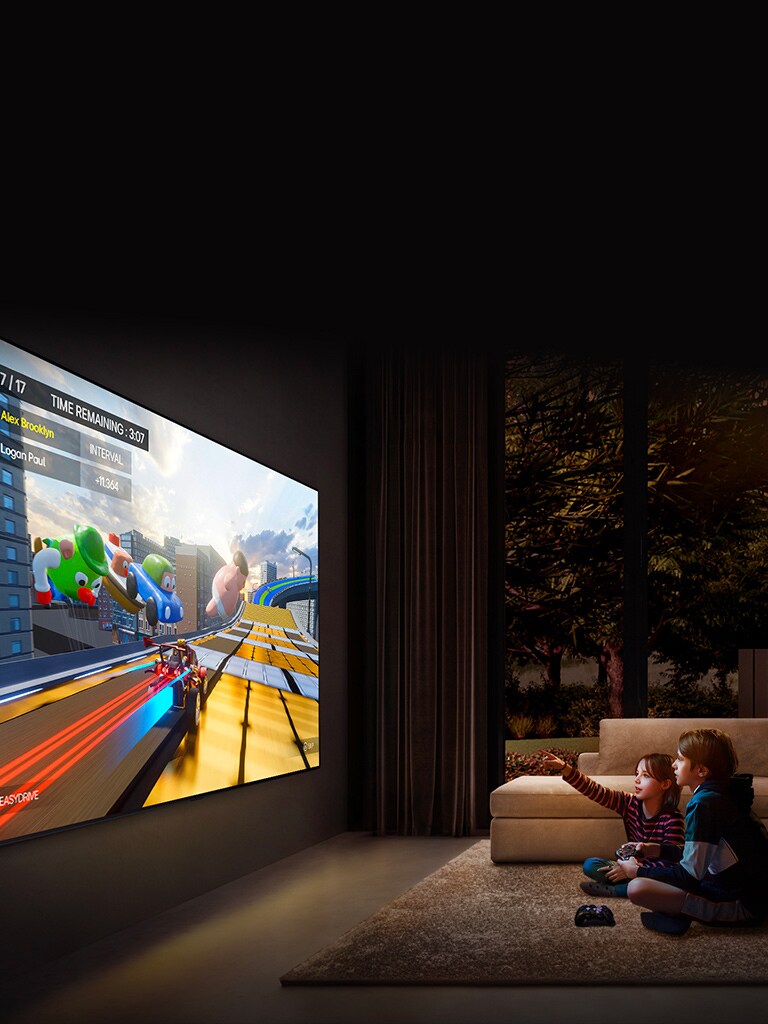 Eine seitliche Ansicht eines wandbefestigten ultragrossen LG TV in einem gemütlichen Wohnzimmer. Es ist ein farbenfrohes Spiel zu sehen und zwei Kinder sitzen auf dem Boden vor dem TV und halten Spielsteuerungen in der Hand.