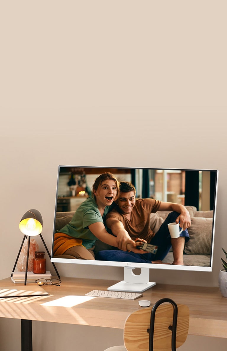 Auf dem Schreibtisch am sonnenbeschienenen Fenster steht ein intelligenter Monitor, auf dessen Bildschirm ein Film zu sehen ist. Neben dem Monitor befinden sich eine Lampe und eine Topfpflanze. Auf dem Schreibtisch befinden sich eine Tastatur und eine Maus.