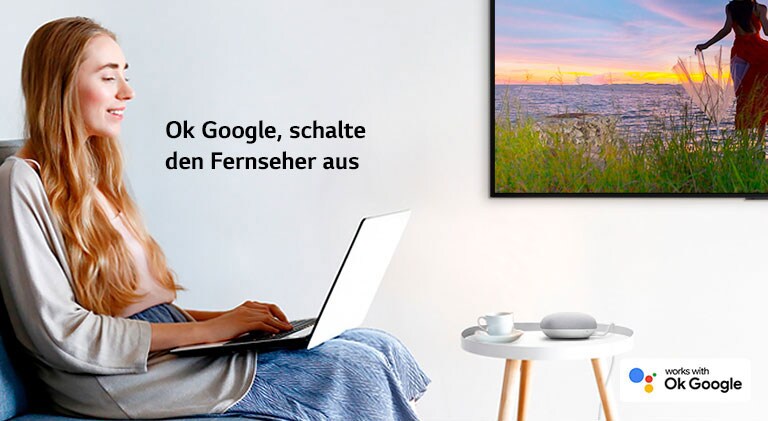 Eine Frau mit einem Laptop sitzt auf einer Couch in einem Raum mit einem Fernseher an der Wand und befiehlt einem Smart Speaker, den Fernseher auszuschalten.