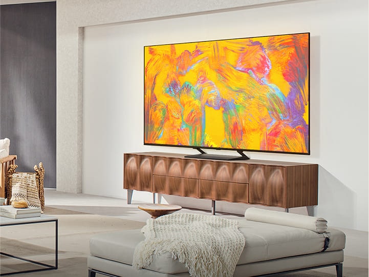 LG QNED TV über einer TV-Schublade in einem gemütlichen Wohnzimmer. Der LG QNED TV zeigt einen abstrakten Hintergrund in Orange, Gelb, Lila und Pink.