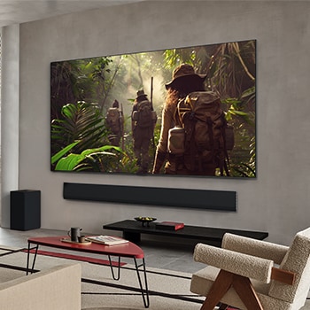 Weite Ansicht eines Wohnzimmers in einem hochwertigen Haus. Ein Mann sieht sich einen Film auf seinem an der Wand montierten LG OLED-Fernseher an. Das Design des Fernsehers fügt sich elegant in die Wand und die Inneneinrichtung ein.