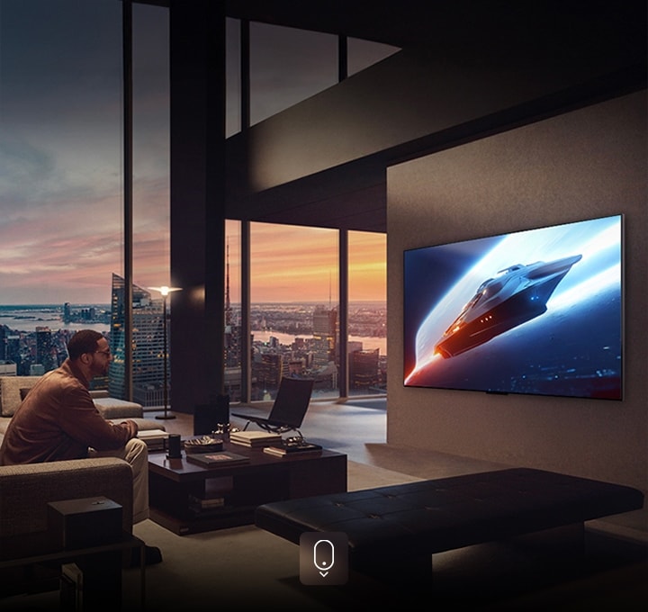 Salon élégant dans un appartement penthouse. Un magnifique paysage urbain visible à l’extérieur de la fenêtre. Un homme assis sur le canapé regarde du contenu sur une TV fixée au mur.