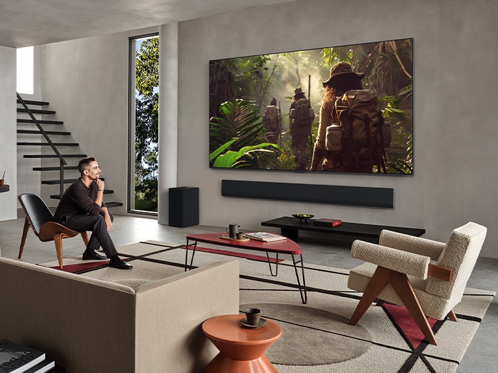 Grand angle de vue d’un salon à l’intérieur d’une maison haut de gamme, un couple regarde un film sur sa LG OLED TV murale. Le design de la TV se fond élégamment avec le mur et la déco intérieure.