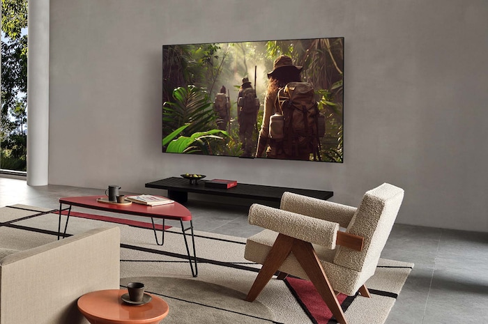 Grand angle de vue d’un salon à l’intérieur d’une maison haut de gamme, un homme regarde un film sur sa LG OLED TV murale. Le design de la TV se fond élégamment avec le mur et la déco intérieure.