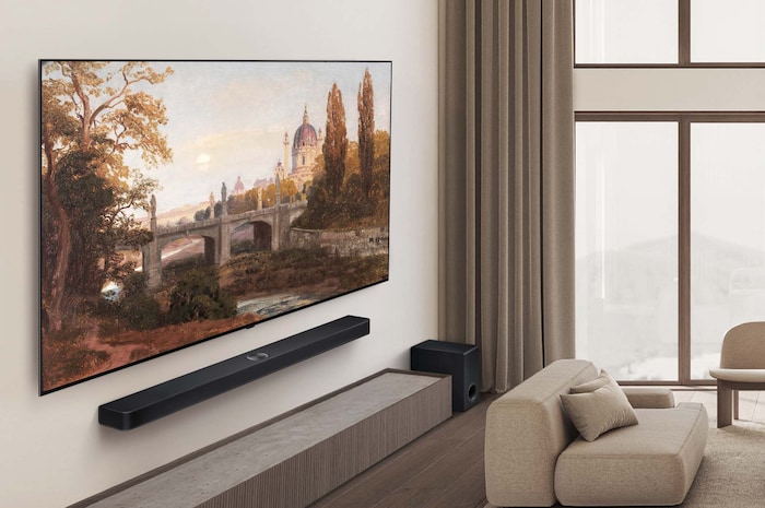 Grand angle de vue d’un salon haut de gamme dans des tons naturels discrets. Sur le mur se trouve une Smart TV LG OLED AI B5 4K avec une œuvre d’art à l’écran. Une LG Soundbar est installée en dessous.