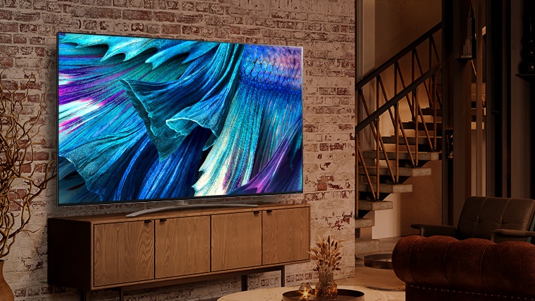 QNED91 installé sur une armoire en bois contre un mur de briques dans un intérieur moderne. L'écran montre une image en gros plan de pétales dans des nuances bleues.