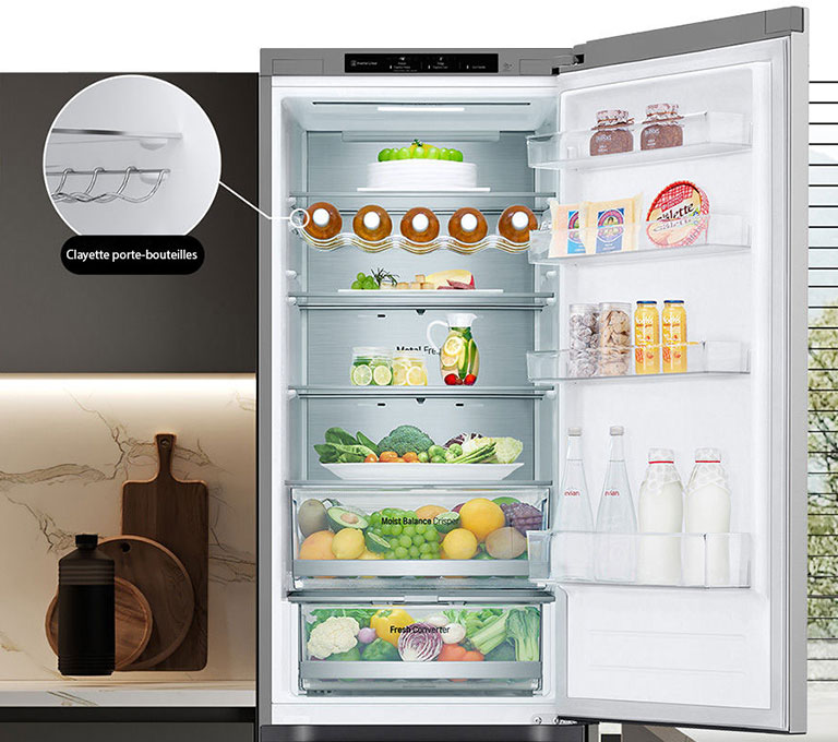 Réfrigérateur rempli d'aliments frais avec porte ouverte présentant un porte-bouteilles et une clayette rétractable.