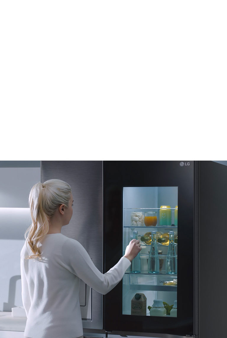 Une vidéo montre une femme qui s’approche de son réfrigérateur InstaView et frappe deux fois. L’intérieur du réfrigérateur s’allume et elle peut voir son contenu sans ouvrir la porte. La vue effectue un zoom avant pour présenter les boissons posées sur la porte, puis un zoom arrière pour voir la femme de derrière alors qu’elle ouvre la porte et prend une boisson.