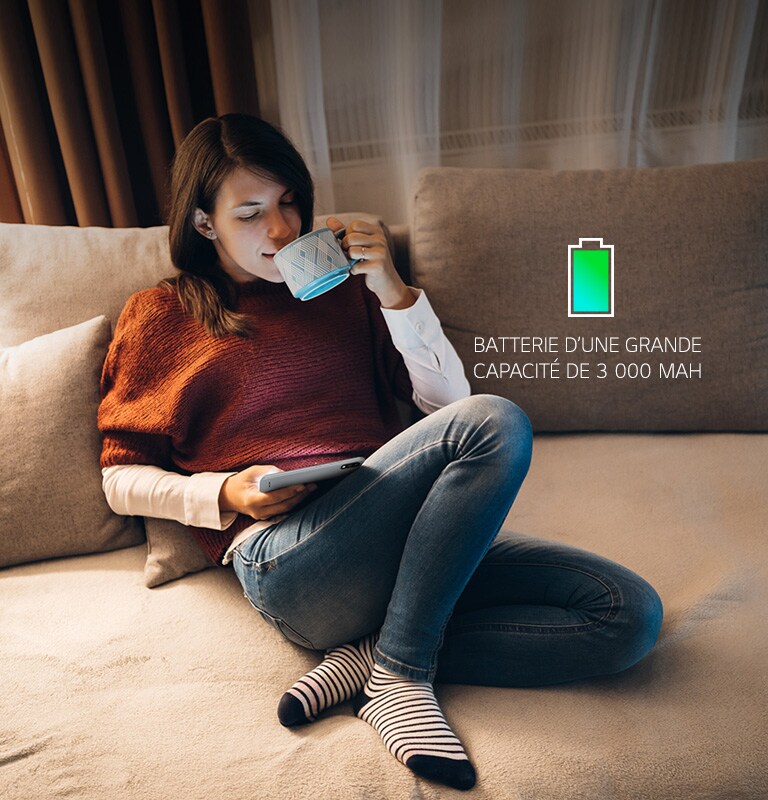 Femme assise sur un canapé, buvant un café et regardant son smartphone