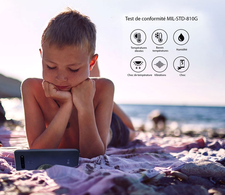 Un enfant allongé sur la plage et regardant un film sur son smartphone