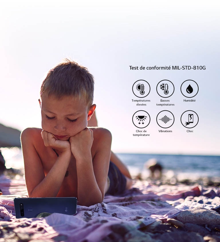 Un enfant allongé sur la plage et regardant un film sur son smartphone