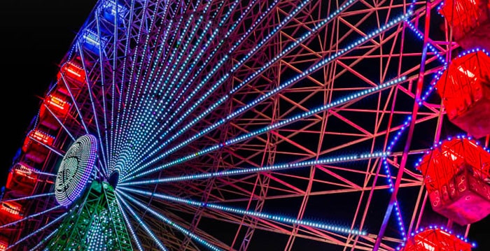 Une grande roue légèrement décolorée s’illumine la nuit, avec des éclats colorés partant du côté gauche de l’écran et se déplaçant sur celui-ci. Au fur et à mesure que les étincelles colorées défilent, l’écran passe d’un voile nuageux à des couleurs éclatantes et lumineuses.
