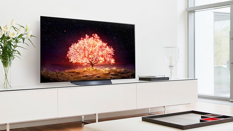 Un téléviseur affichant un arbre brillant orange est placé dans un salon avec intérieur blanc.