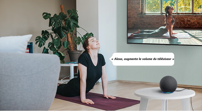 Une femme qui regarde la vidéo de yoga dans le salon commande à une enceinte IA d’augmenter le volume du téléviseur.