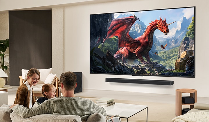 Una familia se sienta en un sofá frente a un televisor LG QNED montado en una pared sobre una barra de sonido LG con una niña señalando una pantalla que muestra dos delfines.